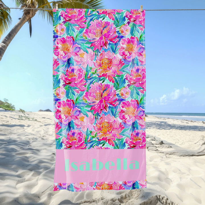 a beach towel with pink flowers on a beach