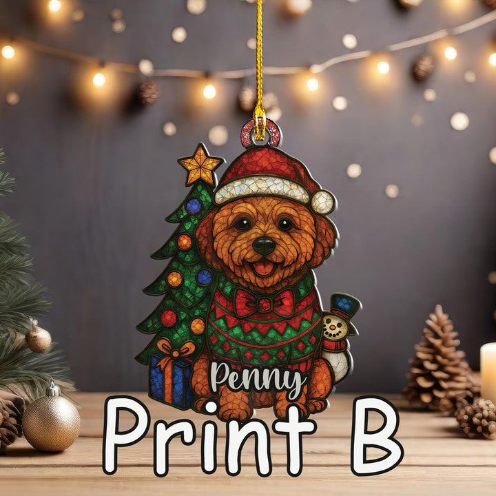 A Christmas ornament featuring a dog wearing a Santa hat and sweater, holding a gift box and a snowman, with the name &quot;Penny&quot; written on it. The ornament is hanging from a string, and there are Christmas lights and pine cones in the background.
